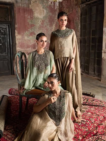 A powerful group shot of three models in earthy-toned cape sets, exuding a sense of modern royalty.