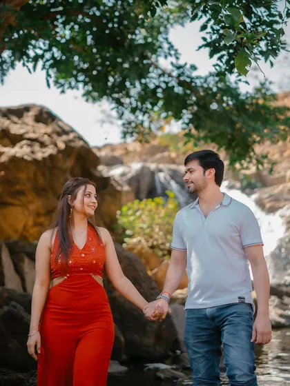 A candid shot of the couple holding hands and sharing a look as they walk by a waterfall.