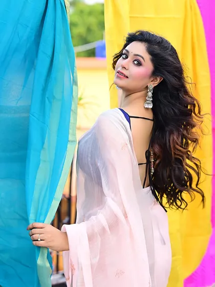 A classic over-the-shoulder pose that is both elegant and alluring. The colorful background contrasts beautifully with the soft pink of the saree, making the whole image pop.