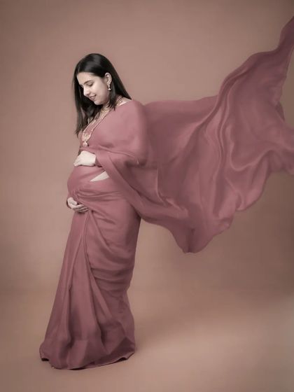 A fine art portrait of a mom-to-be in a dusty rose saree-draped gown. The flowing fabric and her gentle pose create a soft, artistic, and timeless image.