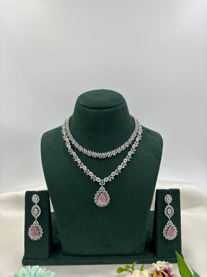 A graceful double-layered AD necklace. The top layer is a simple floral chain, while the bottom layer features a pear-shaped pendant. It is available in white, pink, green, and blue stones.