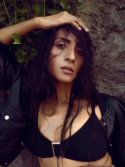 A close-up, wet-look portrait from a moody beach shoot. The model's damp hair and the natural, earthy backdrop create a raw and authentic feel.