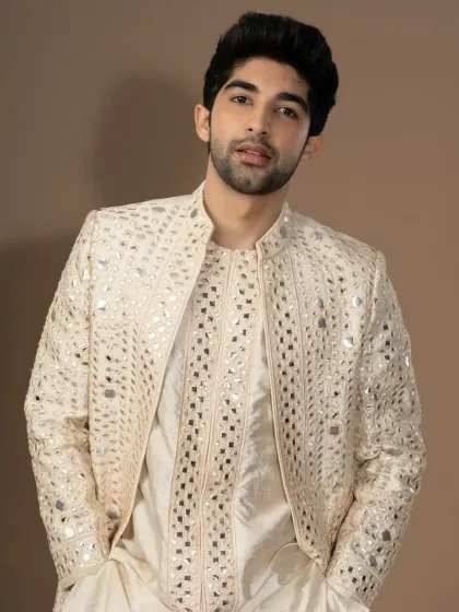 An ivory jacket fully embellished with mirror work, worn over a matching kurta. This creates a dazzling effect for any grand celebration.