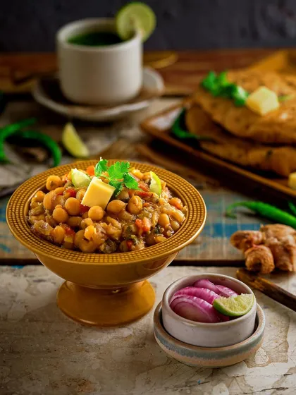 A comforting bowl of Chole Kulche. The image is styled to feel like a classic street-food experience, with pickled onions and a hint of ginger to communicate authentic, robust flavors.
