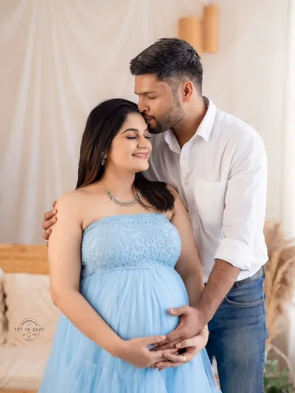 An intimate couple's portrait capturing a sweet forehead kiss. The mom-to-be wears a lovely light blue tulle gown, perfect for our boho-chic studio setup.