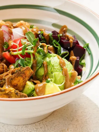 A vibrant and healthy Buddha bowl, packed with fresh vegetables, avocado, and a savory dressing. The bright, natural lighting highlights the freshness of the ingredients.
