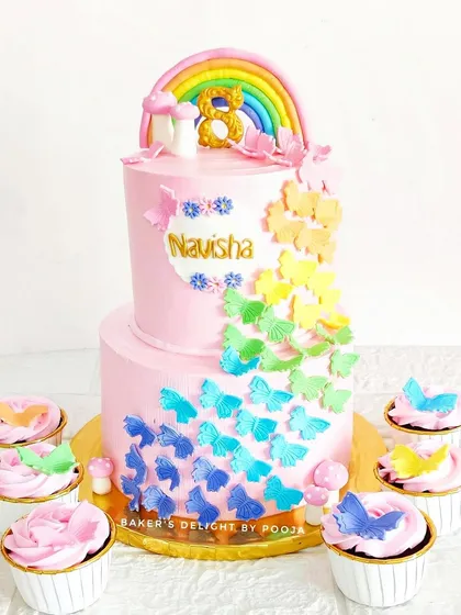 A flutter of magic for an eighth birthday! This two-tier pink butterfly cake is adorned with a cascade of rainbow-colored butterflies and comes with matching cupcakes.
