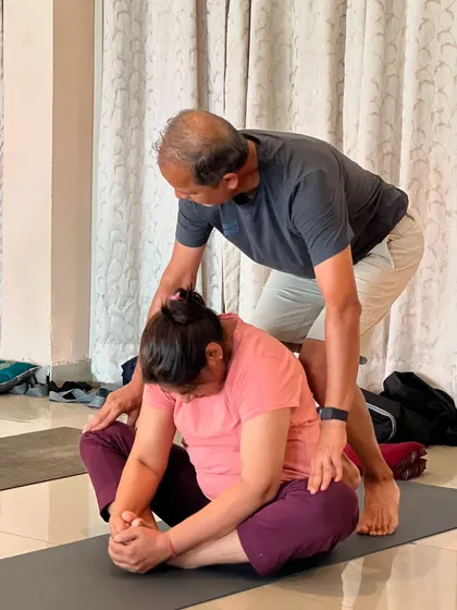 A teacher assists a student in the butterfly pose, helping to release tension in the hips. This is the spirit of our community, always helping each other.