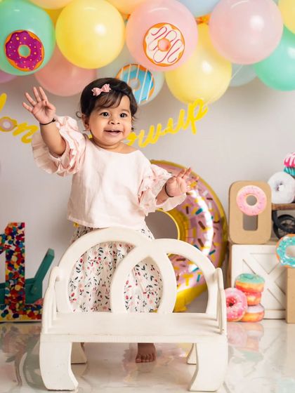 A happy wave from the birthday girl at her 'Donut Grow Up' party. The pastel balloon arch and donut props create a fun and festive atmosphere.