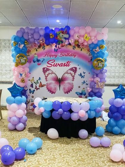 A beautiful butterfly and unicorn themed birthday party with a personalized backdrop and a pastel purple and pink balloon arrangement.