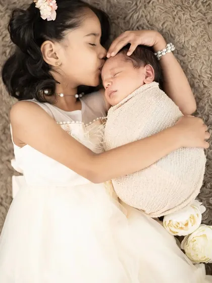 The bond between siblings is so precious. We gently guide these interactions to capture tender moments, like an older sister's protective kiss for her new baby brother.
