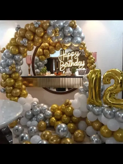 An elegant gold and silver balloon decoration for a 12th birthday. This setup includes a balloon ring, a neon sign, and large foil numbers.