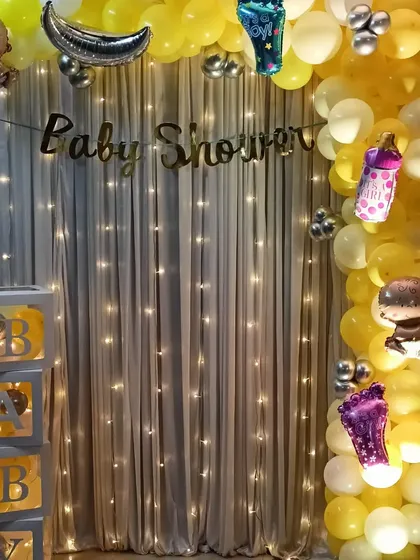 A classic baby shower decoration with a yellow and white color scheme. This setup includes transparent 'BABY' boxes and a fairy light backdrop for a simple yet elegant look.