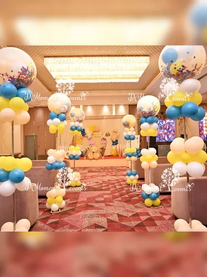 The venue walkway decorated for the "Around the Sun" themed party. Balloon pillars in shades of blue, yellow, and peach line the path, creating a festive and cohesive look throughout the space.