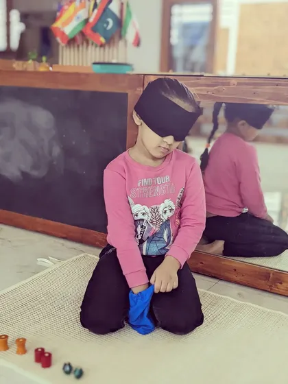 Learning is a sensory experience. This child is using her stereognostic sense, the ability to identify objects by touch alone, while blindfolded. You will learn how to guide children through these powerful sensory explorations that refine their perception and build concentration.