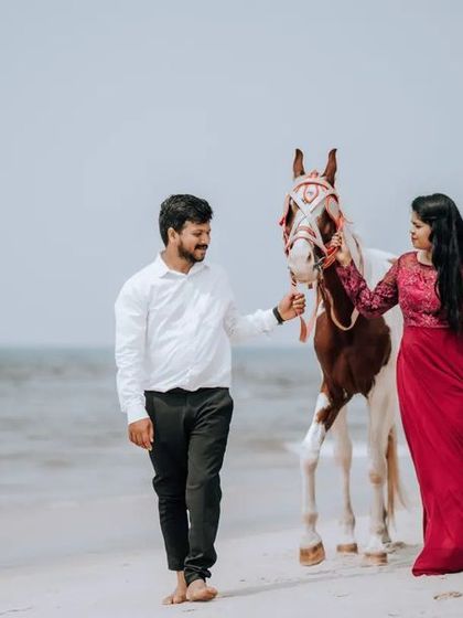 A beautiful shot of a couple walking on the beach with a horse, the bride's red dress creating a stunning contrast against the neutral tones of the sand and sea.