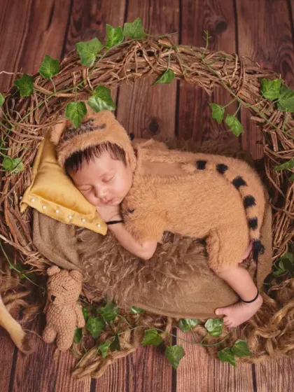 A playful and adorable shot of a newborn in a fuzzy tiger costume, sleeping soundly in a nest-like prop. The jungle-themed setup includes plush animal friends like a tiger and a deer.