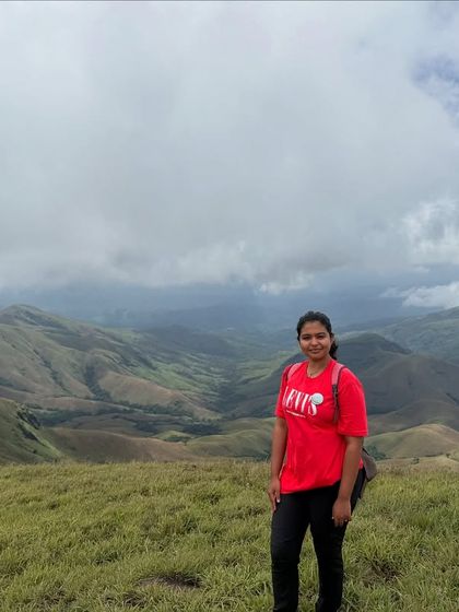 A happy trekker stands against the vast green expanse of Kudremukha, a perfect example of the rewarding views on this trek.
