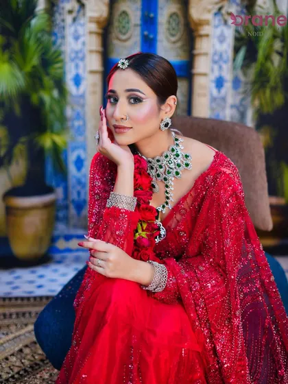 This seated portrait showcases the full bridal attire, from the intricate saree work to the floral hair braid and flawless makeup.