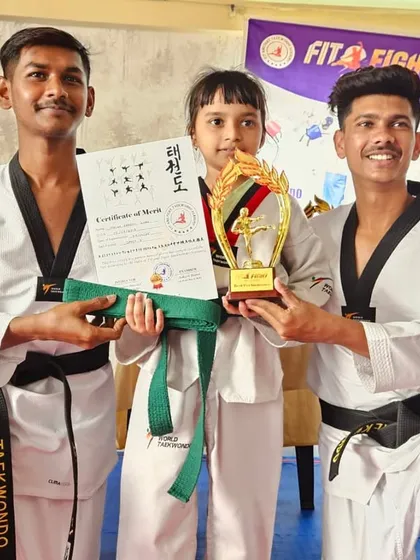 A female student is awarded a large trophy and her new green belt by our coaches, recognizing her hard work and success in the exam.
