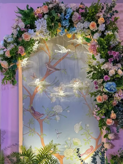 A key decor element: a custom Chinoiserie-print backdrop framed by an arch of pastel pink, peach, and ice blue flowers, with delicate bird hangings.