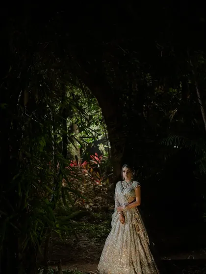 A bride emerging from an enchanted forest. This dramatic, artistic portrait was styled to feel like a page from a dark fairytale. The bride's shimmering silver lehenga creates a magical glow in the moody, natural setting.