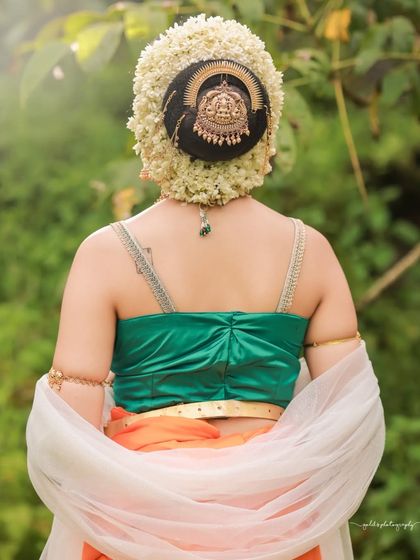 Inspired by the grandeur of Bahubali, this "Sakhi" look features a model in a unique orange and green dhoti-style saree. The outdoor setting and regal jewelry complete the ancient princess aesthetic.