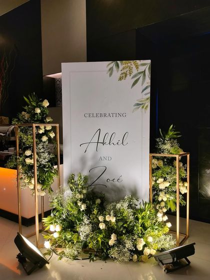 A modern and elegant welcome sign for Akhil and Zoee. The minimalist design with a touch of greenery is flanked by beautiful arrangements of white roses and baby's breath.
