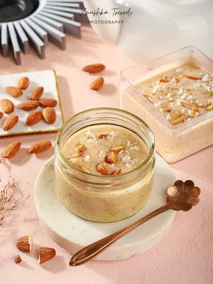 A jar of sweet almond dessert, styled with a soft pink background and a copper spoon. The look is clean, modern, and very appealing.