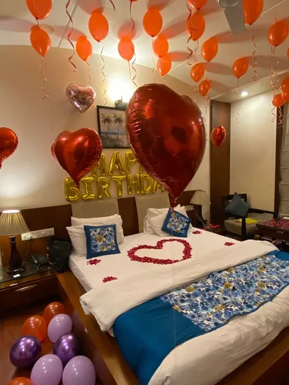 A classic birthday room decoration is always a great choice. This setup features helium balloons on the ceiling, large heart-shaped foil balloons, and a heart made of fresh rose petals on the bed, creating a simple yet beautiful romantic gesture.