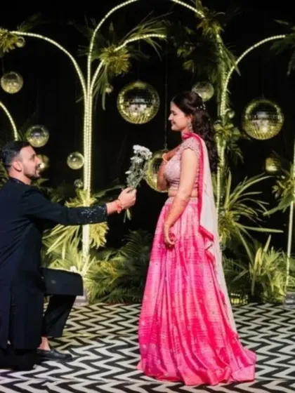 A romantic moment from a Sangeet night. The couple is on a stage with a unique black and white patterned floor and a backdrop of greenery, disco balls, and warm lights.