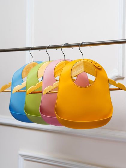 A clean, simple shot of colorful silicone baby bibs hanging on a rack. This is a perfect e-commerce photo that clearly shows the product and color variety.
