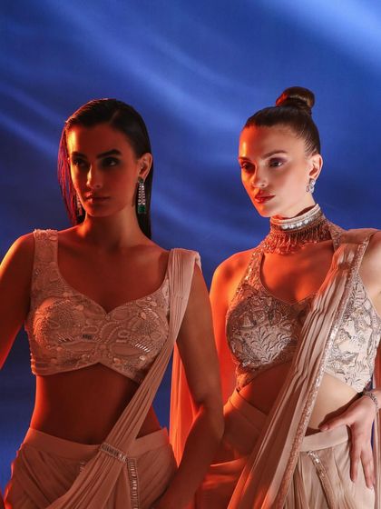 Two models in complementary ivory and beige ensembles. The dramatic lighting with red and blue tones adds an artistic, editorial flair to the shot.