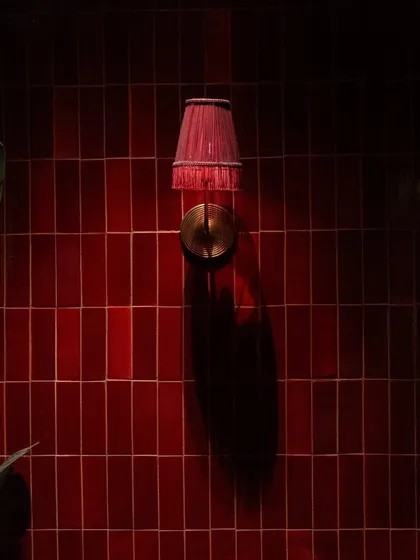 A close-up of the vertically stacked red tiles at Hikki. The deep color and glossy finish interact with the accent lighting to create a rich, dramatic effect.