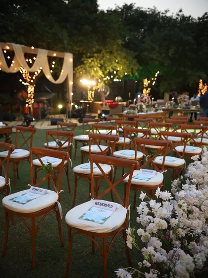 The beauty of an organized setup. Rows of cross-back chairs are perfectly aligned for a ceremony, with a lush border of white flowers creating a defined and elegant aisle.