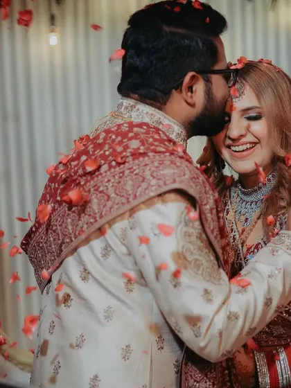 A sweet and tender moment amidst the celebration. The groom's gentle kiss on the bride's forehead, showered in flower petals, is a perfect candid shot full of love.