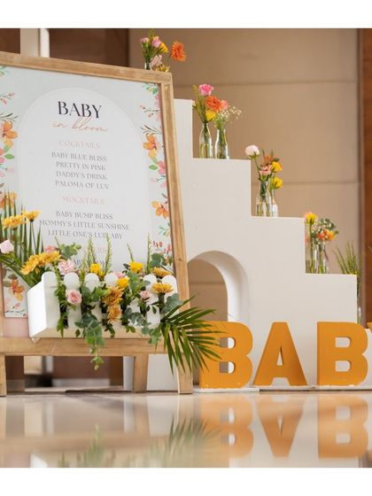 A clear, straight-on shot of the welcome decor, highlighting the modern typography on the sign and the artful arrangement of flowers in and around the display.