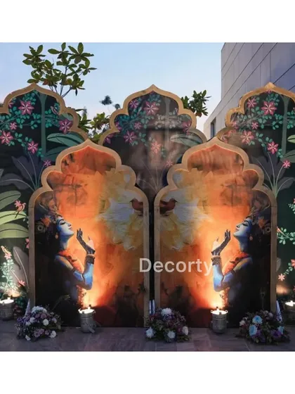 An artistic backdrop featuring panels with paintings of Krishna, framed by floral and foliage designs.