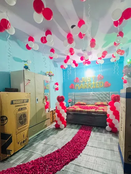 A 'Just Married' room decoration with a rose petal walkway, red and white balloon pillars, and balloons on the ceiling.