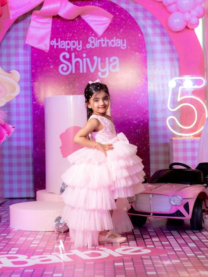 The birthday girl looking fabulous in a pink tiered dress, posing next to her pink toy car at her Barbie party.