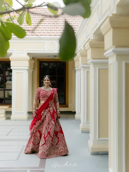 A stunning full-length shot in a classic courtyard. The red of her lehenga and the soft glam of her makeup create a timeless and regal bridal portrait.