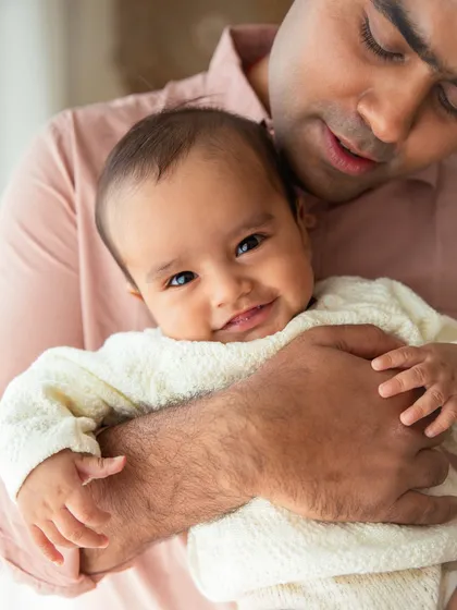 A gentle smile from a 6-month-old baby, held securely in his father's arms. This milestone is perfect for capturing interactive and smiley portraits.