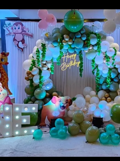 A cute jungle themed birthday party with a circular balloon arch, animal character cutouts, and a large light-up "ONE" sign.