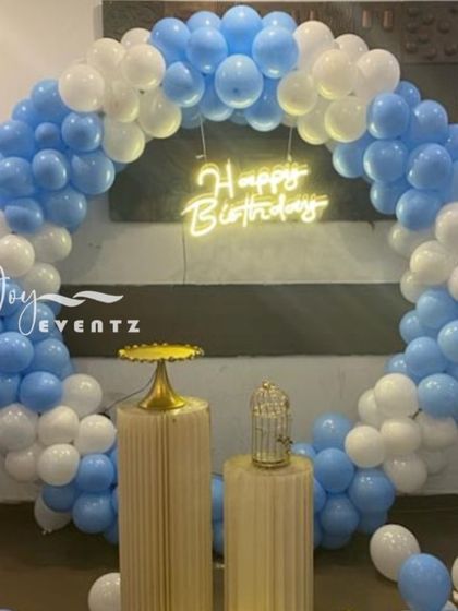 This simple and clean balloon ring decoration is perfect for a celebration at home. The full arch of pastel blue and white balloons creates a beautiful frame, with two fluted plinths ready for the cake and other treats.