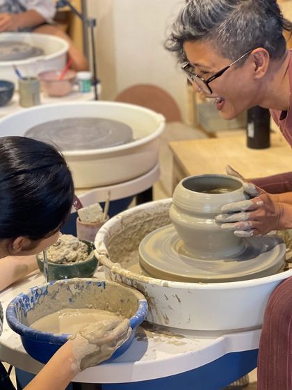 A moment of joy and connection as I share a laugh with a student over a freshly thrown pot.