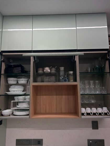 A wide kitchen cabinet with a pull-down shelf mechanism. We organized the glassware and crockery to work with this feature, ensuring everything is secure and easy to reach.