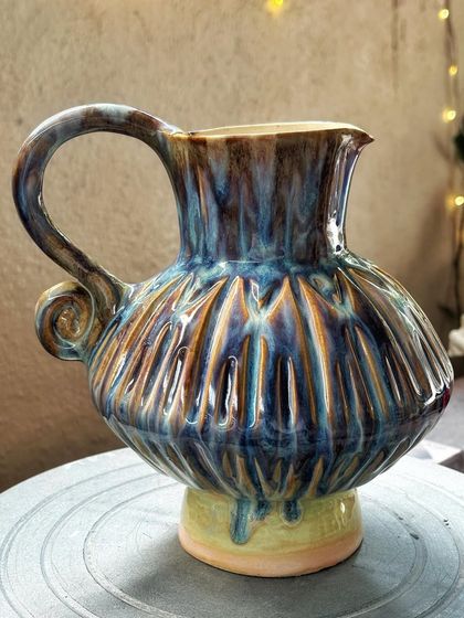 This wheel-thrown pitcher has a wonderfully round, generous shape, perfect for serving water or holding a bouquet of flowers. The textured body and vibrant, layered glazes make it a true statement piece.