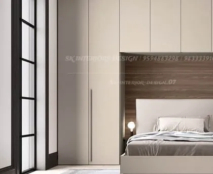 A minimalist bedroom design featuring handle-less, floor-to-ceiling wardrobes and a wood-paneled headboard niche. The clean lines and neutral palette create a tranquil and modern space.