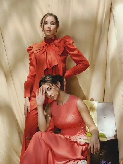 A powerful and artistic pose. The makeup for both models is kept soft and neutral, allowing the bold colors of their outfits and their expressions to be the focus of the shot.