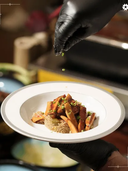 A chef's final touch, sprinkling fresh greens on a plated dish. This moment captures the care and precision that goes into every single plate we serve.